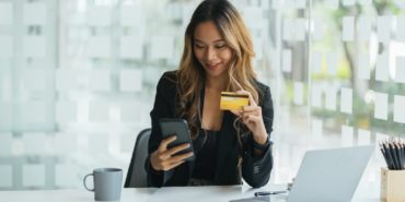 Young asian business woman using smart phone and holding credit card while online shopping and payment online with laptop computer on desk at home, female holding debit card, communication concept.