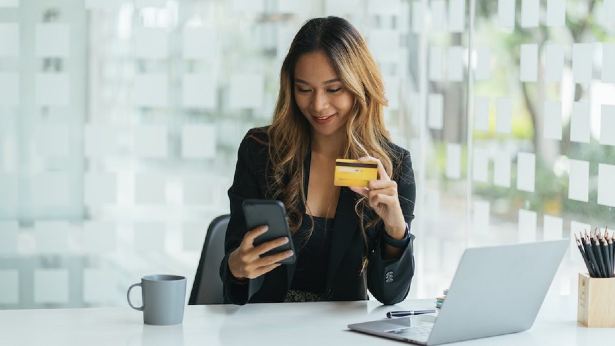 Young asian business woman using smart phone and holding credit card while online shopping and payment online with laptop computer on desk at home, female holding debit card, communication concept.
